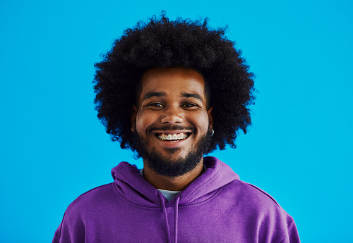 Front view of a young black man with a afro hairstyle looking into the camera, smiling with copy space, stock photo