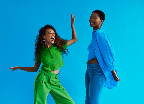 Two young black women standing and dancing, wearing casual clothing whilst laughing with their hands raised wearing casual clothing with copy space, stock photo