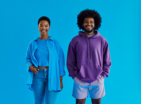 Happy young black couple standing facing the front whilst looking into the camera smiling wearing casual clothing with their hands in there pocket with copy space, stock photo