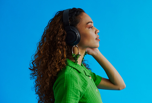 Young multiracial woman standing whilst turned to the side looking and listening to music through her headphones with copy space, stock photo