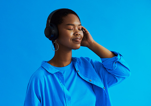 Young black woman smiling  with her eyes closed whilst holding her headphones as she listens to music with copy space, stock photo