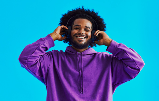 Front view shot of a black man standing whilst listening to music, holding his headphones whilst smiling with copy space, stock photo
