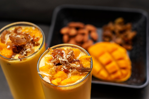 Mango lassi or mango yogurt smoothie garnished with mango slice and chopped nuts a popular drink in India.