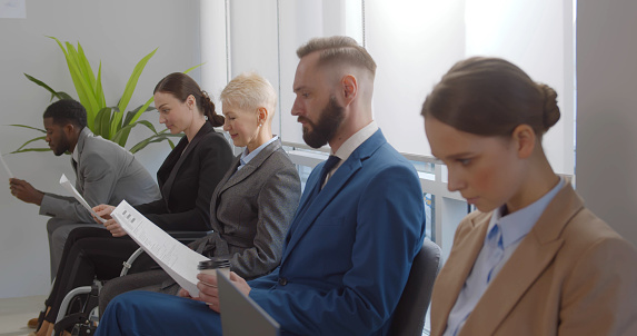 Young woman in wheelchair waiting in line for job interview in office corridor. Disabled female job applicant in office corridor waiting in row for business meeting with employer