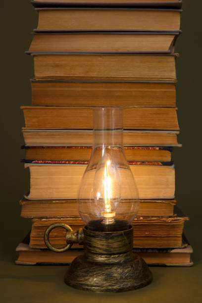 istock Old books and a lamp with a burning light on an olive background. 1491518082
