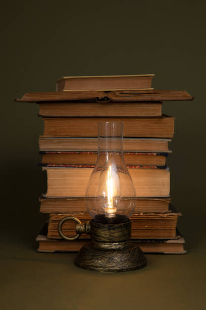 istock Old books and a lamp with a burning light on an olive background. 1491518434