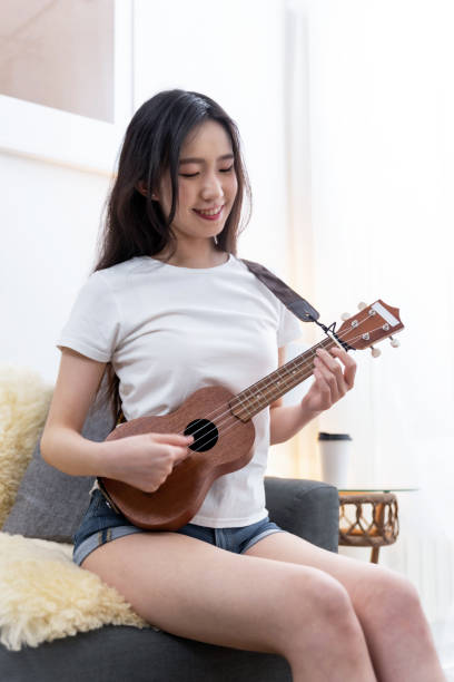 istock Young woman playing ukelele sitting on sofa at home 1491518557