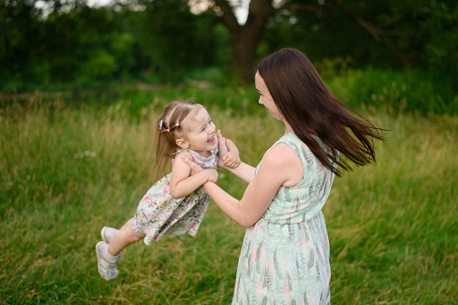 Portraits of a joyful mother and daughter spend time together, smile, have fun, enjoy happy family time and lift her up in the air in the park. Motherhood, lifestyle. Mothers Day