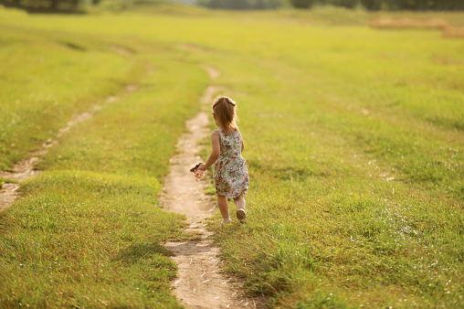 Portrait of a girl in a summer dress running across the field in summer. Concentration of children and nature, fun summer activities. Freedom. View from the back. Copy space.