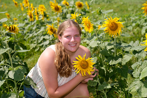Teenaged girl standing in a field of sunflowers.