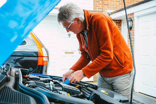 Color image depicting a man checking and maintaining the engine of his car, making sure everything is in working order.