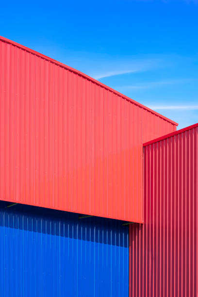 rote und blaue wellblech-lagerhaushauswand im modernen minimalistischen stil vor blauem himmelshintergrund im vertikalen rahmen - architecture roof aluminum sheet industry stock-fotos und bilder