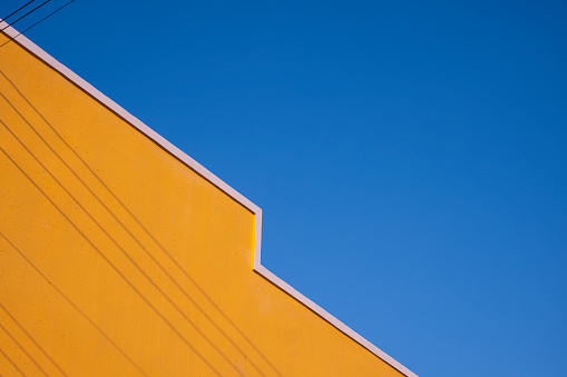 Street Minimal Architecture style of colorful yellow Building Wall with shadow of electric cable lines on surface against blue clear sky Background