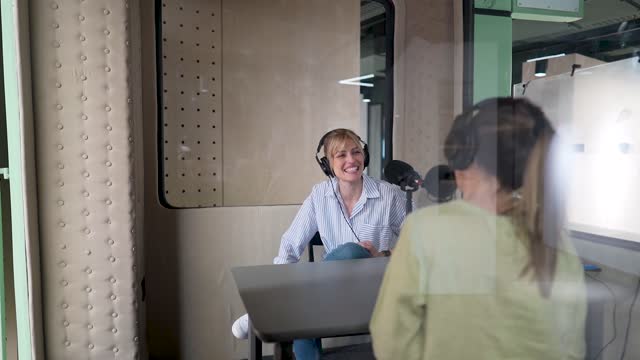 Two female podcast hosts recording content in a soundproof broadcasting room