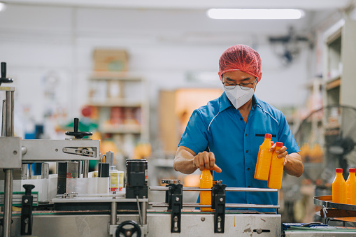 Asian Chinese production line worker picking up and examining orange juice bottle before packing