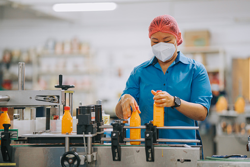Asian Chinese production line worker picking up and examining orange juice bottle before packing