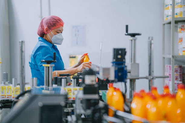 istock Asian Chinese production line worker picking up and examining orange juice bottle before packing 1491529171