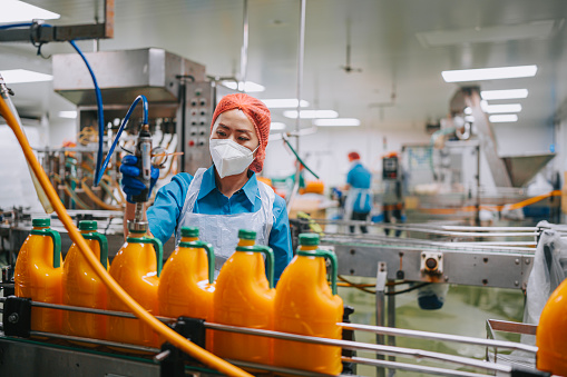 Asian Chinese female orange juice factory worker sealing bottle cap of orange juice in production line