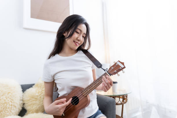 istock Young woman playing ukelele sitting on sofa at home 1491529308