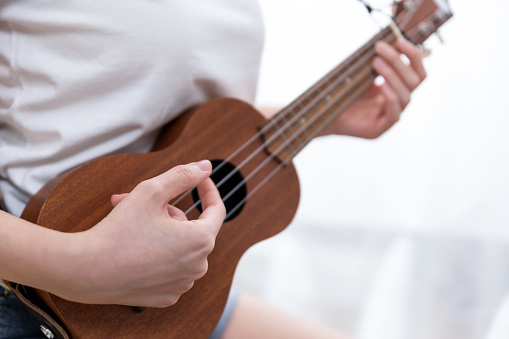 Young woman playing ukelele sitting on sofa at home