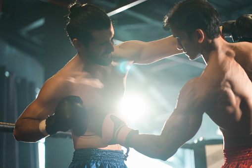 Two professional boxers are fighting on boxing ring, sportsmen boxing in the fight on square stage, or sport exercising with trainer at boxing and self defense lesson studio background, Thai Box match