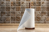 Paper towels on a wooden holder on the table against the background of a tiled wall.