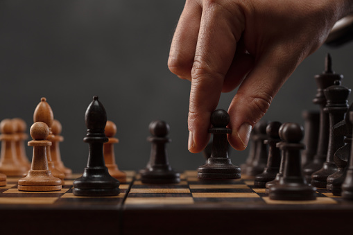 Chess pieces on the board. Chess player makes a move the black pawn forward. Game of chess. Strategy, management or leadership concept. Shallow depth of field