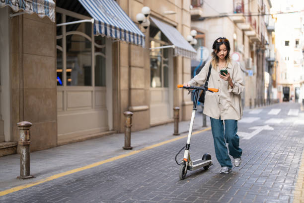 istock Female student of Chinese ethnicity commuting with electric push scoter while using mobile phone 1491532254