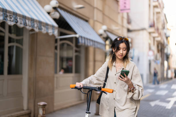 istock Modern woman Chinese ethnicity commuting with electric push scoter while using mobile phone 1491532277
