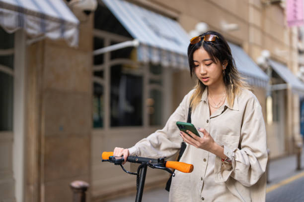 istock Modern woman Asian ethnicity commuting with electric push scoter while using mobile phone 1491532311