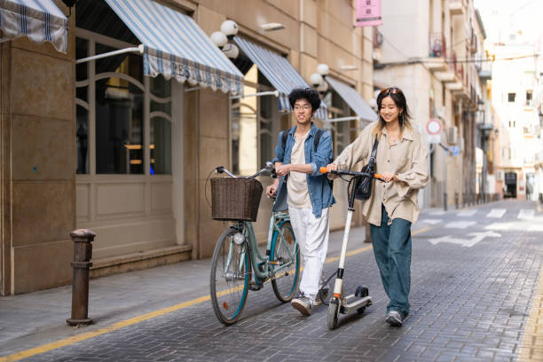 Asian female and male students, commuting together with bicycle and electric push scooter stock photo