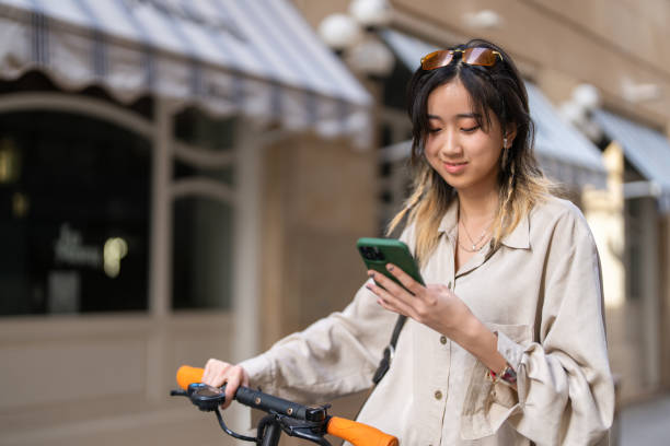 istock Female student of Chinese ethnicity commuting with electric push scoter while using mobile phone 1491532409