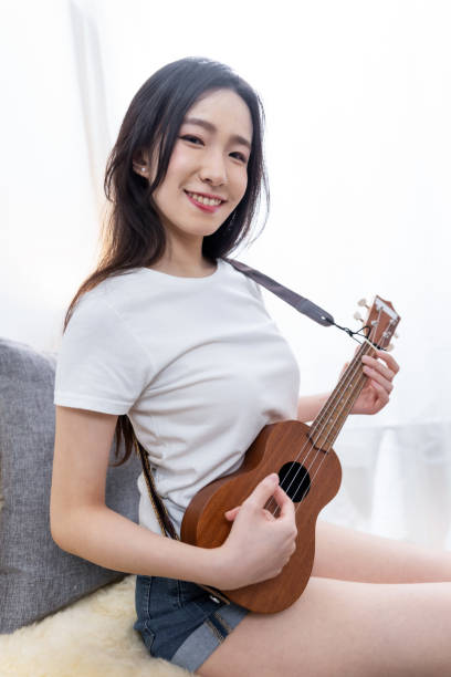 istock Young woman playing ukelele sitting on sofa at home 1491534153