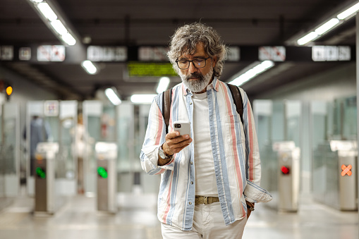 Shot of a modern senior man walking and using smart phone