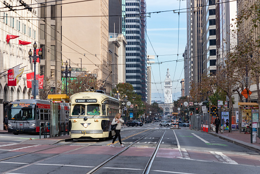 San Francisco, United States - November 27, 2022: A picture of Market Street in San Francisco, with the Ferry Building at the far right, and a bus and a street car on the left.