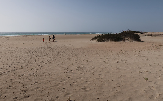 Three distant people on near empty idyllic Grandes beach. Corralejo dunes National Park.  South west of the town. Fuerteventura, Canary Islands, May 2023.