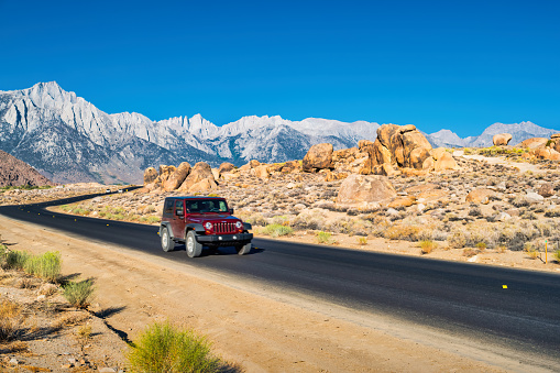 SUV drives on Whitney Portal Road with the Sierra Nevada and Mount Whitney in the background in California, USA on a sunny day.
