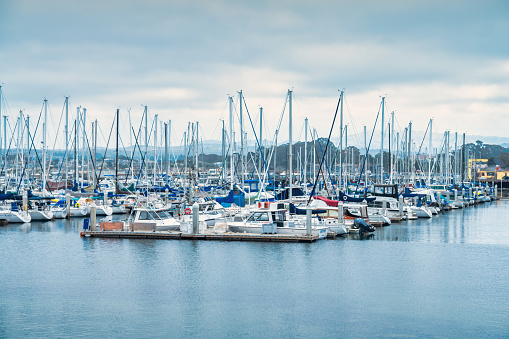 Sailboats are docked at a marina in Monterey, California, USA on an overcast day.