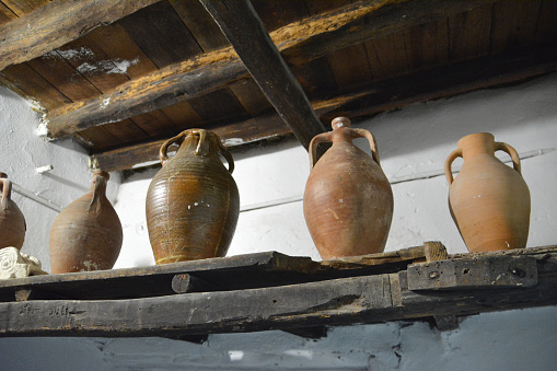 A wooden shelf with many clay jugs on it for olive oil