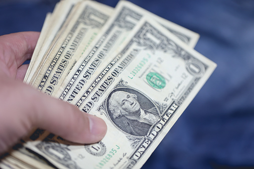 A man holding one dollar bills. Close-up photo. Blue background.