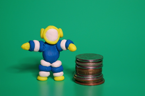 A toy astronaut and coins on a green background. Finance and economics.