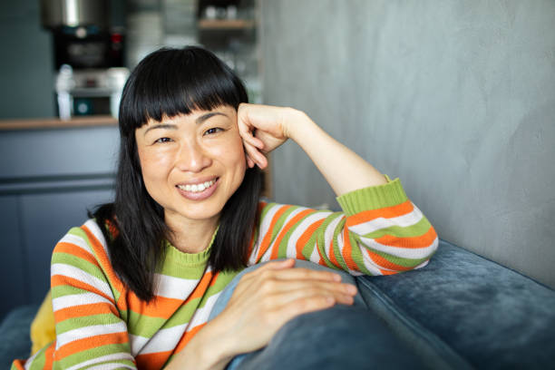 istock Young Japanese woman smiling while sitting on a couch and looking at the camera 1491549657