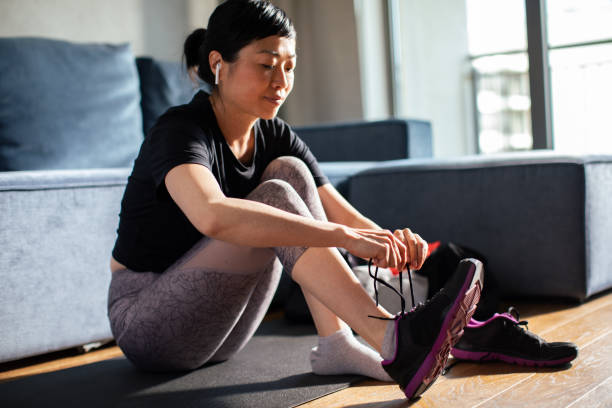 Young Japanese woman tying her shoelaces and getting ready to go exercise Close up of a Young Japanese woman tying her shoelaces and getting ready to go exercise home workout stock pictures, royalty-free photos & images