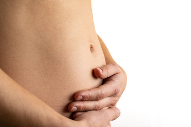 Very close up view of woman in first months of pregnancy gently holding her belly. Pregnancy first trimester - week 18. Close up. Side view. White background. Bright shot. Description: Very close up view of woman in first months of pregnancy gently holding her belly. Pregnancy first trimester - week 18. Close up. Side view. White background. Bright shot. stomach knot stock pictures, royalty-free photos & images