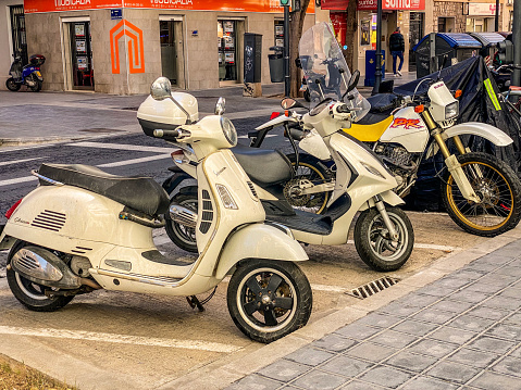 Valencia, Spain - March 6, 2023: Group of scooters and bikes in the street next to the sidewalk. The use of this mode of transport became so widespread that the government created dedicated spaces to park them