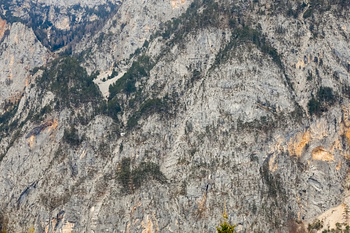 A section of a steep rocky slope that is covered with trees in places as seen from somewhere in Arnoldstein, Austria