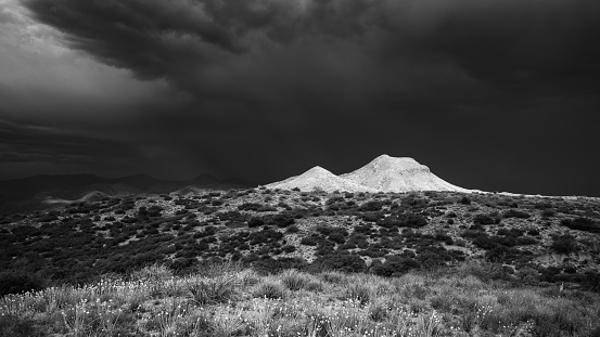 A May monsoon provides dramatic lighting on high desert hills with looming thunderstorm in distance