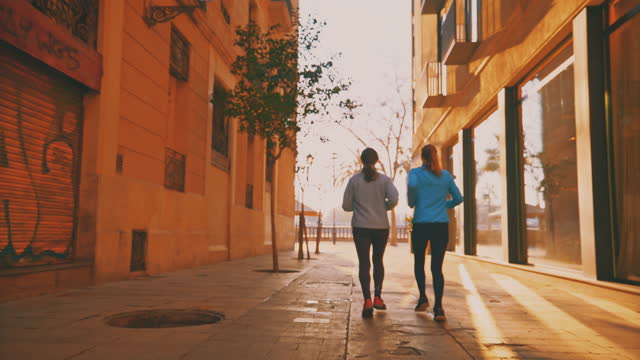 Slow motion shot of female friends running in narrow alley. Women are jogging amidst buildings. They are living healthy lifestyle.