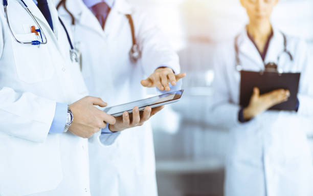istock Group of unknown doctors  use a computer tablet to check up some medical names records, while standing in a sunny hospital office. Physicians ready to examine and help patients. Medical help, insuranc 1491564861