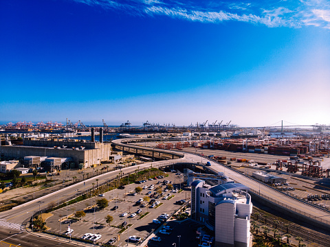 From high above, the aerial view unveils a sprawling tapestry of industry and commerce: the Port of Los Angeles shipping yard. Stretching out as far as the eye can see, it is a bustling hive of activity, an intricate labyrinth of containers, cranes, and vessels.\n\nLike colorful building blocks, countless cargo containers are stacked meticulously, forming towering walls that seemingly reach for the sky. The containers create a mosaic of vibrant hues, as reds, blues, greens, and yellows intermingle in an organized chaos. These rectangular giants house goods from around the world, awaiting their journey to various destinations.\n\nGiant cranes, like gentle giants, dance along the dockside, their long arms gracefully lifting and moving containers with precision and efficiency. The cranes become a symphony of motion, orchestrating the synchronized ballet of unloading and loading ships, their mechanical grace a testament to human ingenuity.\n\nMassive cargo ships, like floating cities, dot the harbor, their sheer size awe-inspiring. Their towering decks and smokestacks cast shadows over the shimmering water below. Tugs and pilot boats bustle around them, guiding their immense presence with skilled navigation.\n\nIntricate networks of roads and rail lines weave through the shipping yard, connecting the port to the broader transportation infrastructure. Trucks and trains tirelessly shuttle goods to and from the port, forming an essential link in the global supply chain.\n\nAmidst this industrial landscape, the port's waterfront promenade provides a contrast of calm and leisure. Strolling pedestrians and cyclists enjoy the fresh sea breeze, soaking in the atmosphere and marveling at the scale of operations before them.\n\nThe aerial view of the Port of Los Angeles shipping yard is a testament to the interconnectedness of the global economy, where goods and products traverse vast distances, weaving a tapestry of trade and commerce that fuels the modern world.
